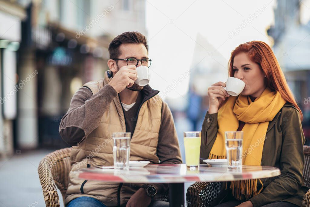 Attractive young couple in love sitting at the cafe table outdoors, drinking coffee