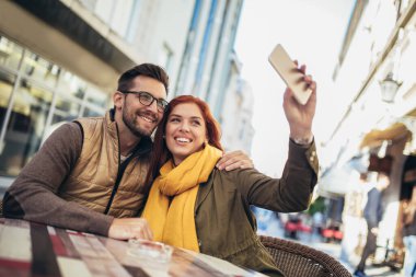 Happy young couple using a phone together at a coffee shop, make selfie photo.