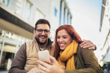 Happy young couple using a phone together at a coffee shop. Young man and woman looking at touch screen computer and smiling.
