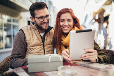 Happy young couple using a digital tablet together at a coffee shop. Young man and woman looking at touch screen computer and smiling.