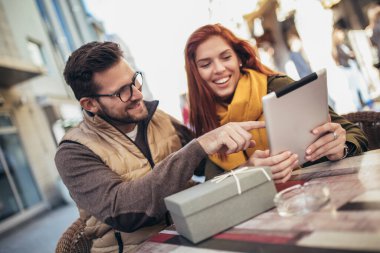 Happy young couple using a digital tablet together at a coffee shop. Young man and woman looking at touch screen computer and smiling.
