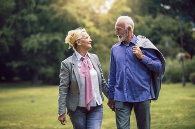 Aktif kıdemli beyaz çift, öğleden sonra parkta el ele tutuşurken mutlu görünüyorlar.