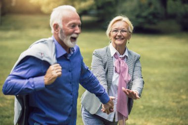 Aktif kıdemli beyaz çift, öğleden sonra parkta el ele tutuşurken mutlu görünüyorlar.