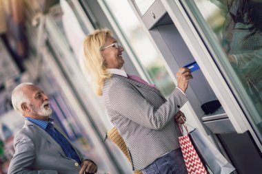 Senior couple with shopping bags using cash machine
