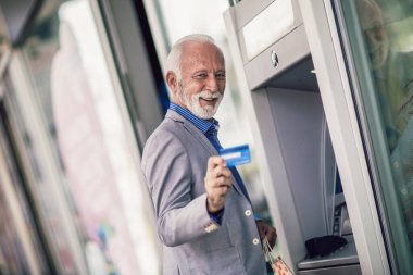 Senior man using ATM machine with credit card.