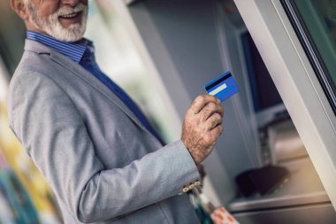 Senior man using ATM machine with credit card.