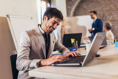 Mutlu iş adamı dizüstü bilgisayar kullanıyor ve arka planda takım projesi tartışıyor..