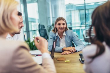 Office colleagues having discussion during meeting in conference room. Group of men and women sitting in conference room and smiling.