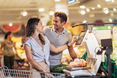 Young couple putting fruits on scale in supermarket