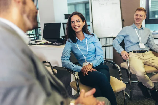 Confident young businesswoman with accreditation badge around her neck talking with colleague at business event