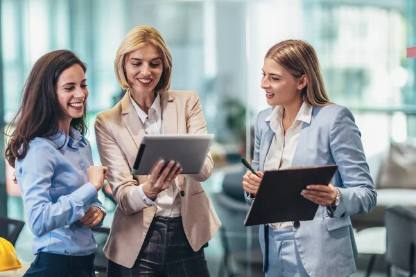 Three businesswomen talking in the office. Happy business colleagues using digital tablet while standing in a office