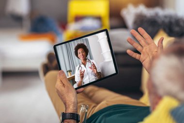 Beyaz erkek, Evdeki Oturma Odası 'ndaki Dijital Tablet' ten Tıbbi Danışmanına bir video görüşmesi yapıyor.