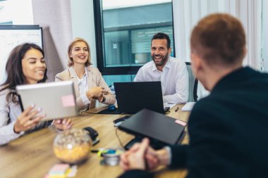 Office colleagues having discussion during meeting in conference room. Group of men and women sitting in conference room and smiling.