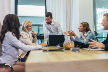 Office colleagues having discussion during meeting in conference room. Group of men and women sitting in conference room and smiling.