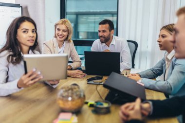 Office colleagues having discussion during meeting in conference room. Group of men and women sitting in conference room and smiling.