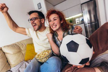 Mutlu genç çift hafta sonunu evde, kanepede oturup televizyonda futbol izleyerek ve favori takım için tezahürat yaparak geçiriyor.