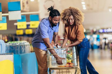African American couple with trolley purchasing groceries at mall