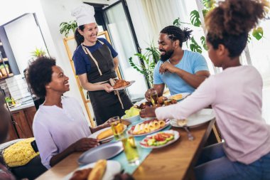 Yemek masasında yemek yiyen çok nesilli Afro-Amerikan bir aile. Beyaz kadın aşçı servis ediyor..