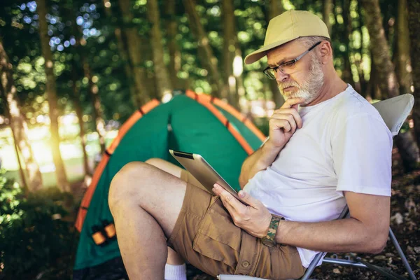 成熟した男はテントの前に座って デジタルタブレットを使用して — ストック写真