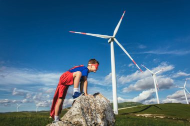 Süper kahraman çocuk rüzgar çiftliğinin önünde. Küçük çocuk süper kahramanı oynuyor..