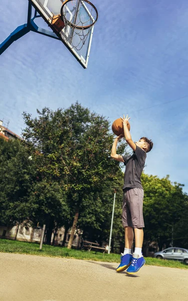 可愛いです男の子でグレーTシャツは市内の遊び場でバスケットボールをプレイ — ストック写真