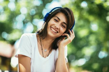 Genç kadın parkta kulaklıkla müzik dinliyor.