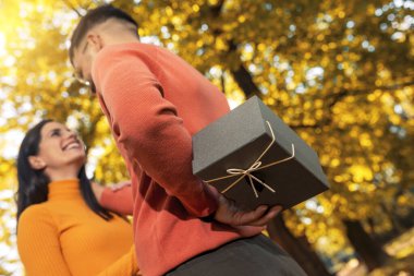 Kafkasyalı erkek arkadaş, sonbahar parkında sevgililer günü için sevgililer günü hediyesi olarak güzel sevgilisine bir kutu hediye verdi.