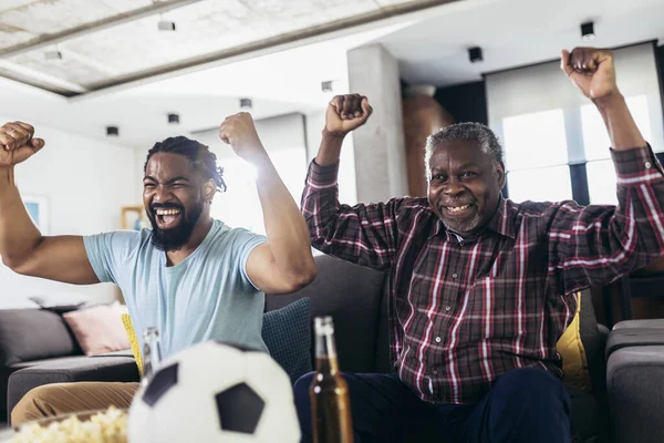 Man relax on sofa in living room with senior father scream support favorite sports team together