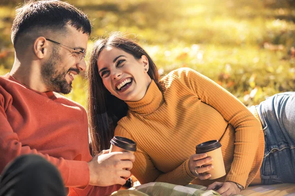 若い男と女は秋に公園の毛布の上に座ってコーヒーを飲む — ストック写真