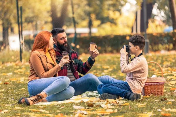 年轻快乐的父母在秋天的一天和他们的儿子在公园里玩得开心 男孩在野餐时给他的父母拍照 — 图库照片