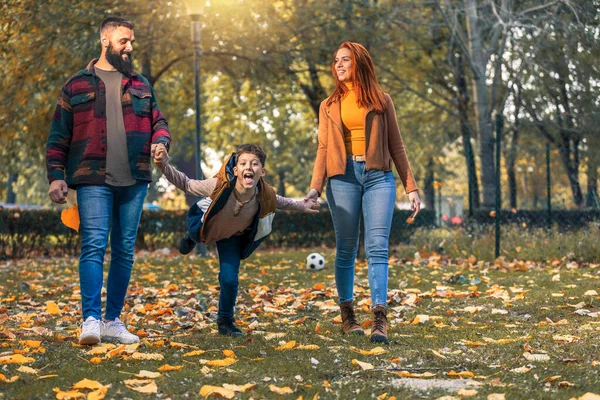 秋の日に公園を走りながら楽しい時間を過ごしている若い幸せな両親 — ストック写真