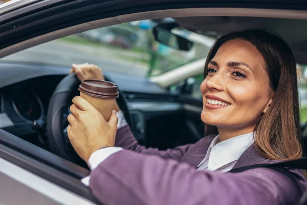 車で運転している若いビジネスマンは 昼間は車から手を引いてコーヒーを飲んでいる — ストック写真