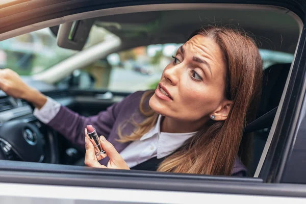 Young businesswoman fixing make-up in a car in the traffic jam