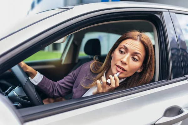 Young businesswoman fixing make-up in a car in the traffic jam