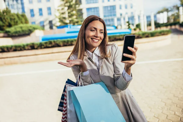市内で買い物をしながら携帯電話を外で使う魅力的な若い女性 — ストック写真