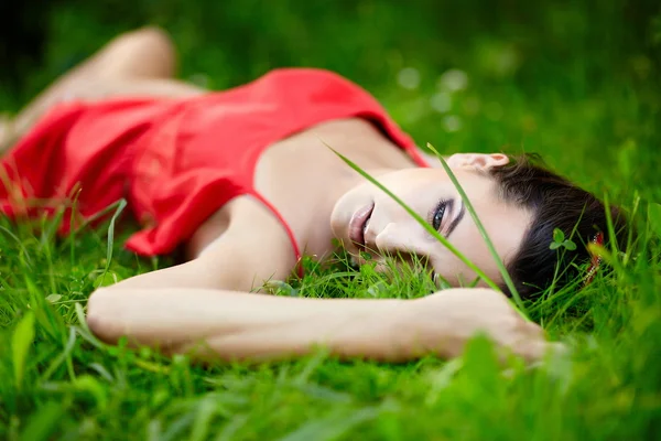 赤いドレスを着て公園に緑の夏の明るい草で横になっている女の子 — ストック写真