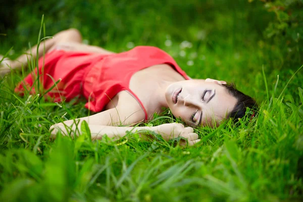 Dziewczyna leży w lato zielony jasny trawa w parku w czerwonej sukience — Zdjęcie stockowe