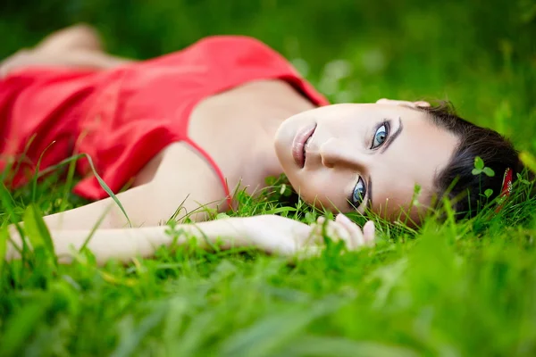 Chica acostada en verde verano hierba brillante en el parque en vestido rojo —  Fotos de Stock