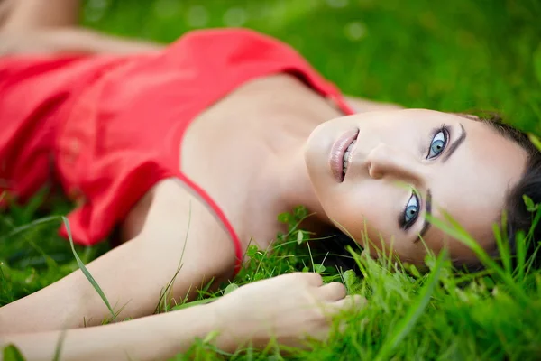 Chica acostada en verde verano hierba brillante en el parque en vestido rojo — Foto de Stock