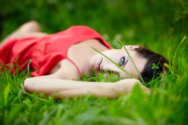 Girl lying in green summer bright grass in the park in red dress — Stock Photo, Image