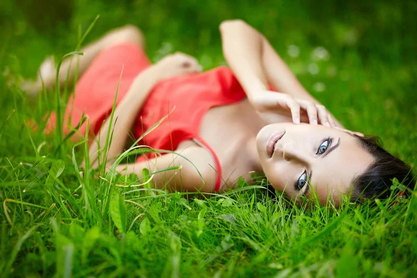 Girl lying in green summer bright grass in the park in red dress Stock Photo