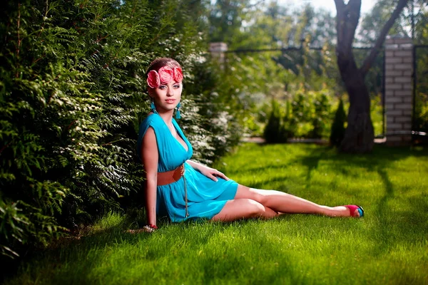 Mulher em vestido azul brilhante posando ao ar livre sentado na grama verde — Fotografia de Stock