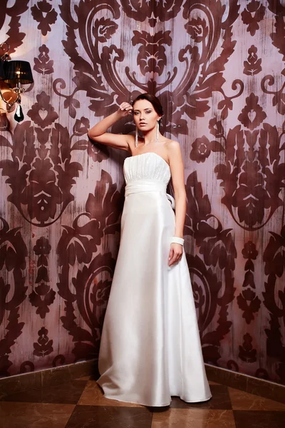 Joyeux belle mariée sexy fille brune femme en robe de mariée blanche avec coiffure et maquillage lumineux à l'intérieur — Photo