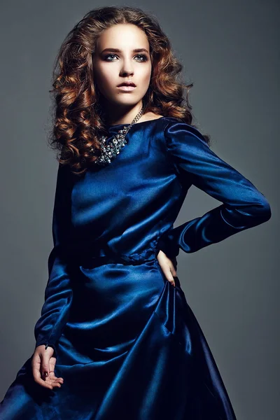 Alta moda look.glamor retrato de hermosa sexy elegante morena modelo de mujer joven caucásica con maquillaje brillante, con cabello rizado saludable en vestido azul brillante en el estudio — Foto de Stock