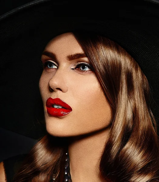 High fashion look.glamor close seup portrait of beautiful sexy stylish Caucasian young woman model with bright makeup, with red lips, with perfect clean skin in big black hat — стоковое фото