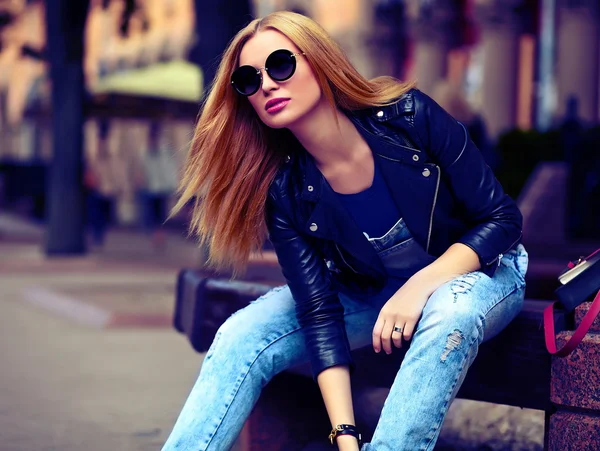 Retrato de lindo divertido moderno sexy urbano joven elegante mujer sonriente modelo de niña en tela moderna brillante al aire libre sentado en el parque en jeans en un banco en gafas —  Fotos de Stock