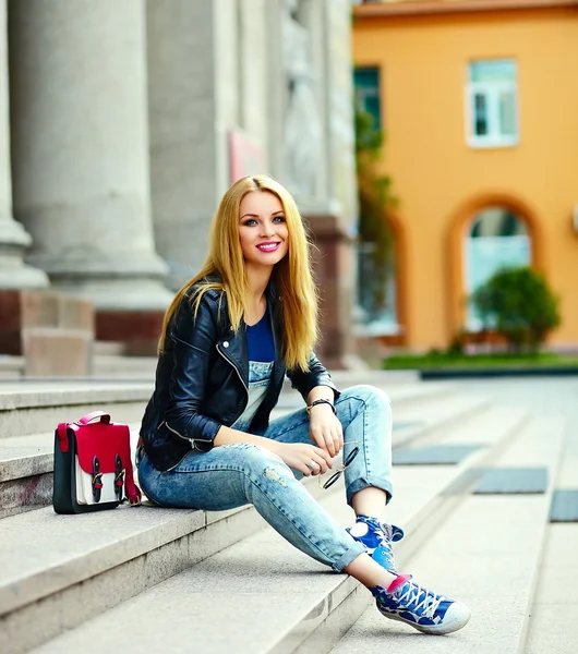 Retrato de bonito engraçado moderno sexy urbano jovem elegante sorridente mulher menina modelo em pano moderno brilhante ao ar livre sentado no parque em jeans em um banco de óculos com saco rosa — Fotografia de Stock