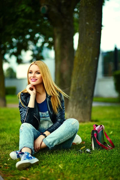 Retrato de bonito engraçado loiro moderno sexy urbano jovem elegante sorridente mulher menina modelo em brilhante pano moderno ao ar livre sentado no parque em jeans com saco rosa — Fotografia de Stock