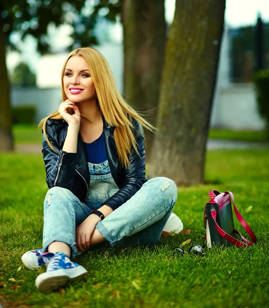 Retrato de lindo divertido rubio moderno sexy urbano joven elegante mujer sonriente modelo de niña en tela moderna brillante al aire libre sentado en el parque en jeans con bolsa de color rosa — Foto de Stock