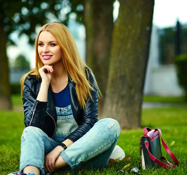 Retrato de lindo divertido rubio moderno sexy urbano joven elegante mujer sonriente modelo de niña en tela moderna brillante al aire libre sentado en el parque en jeans con bolsa de color rosa — Foto de Stock